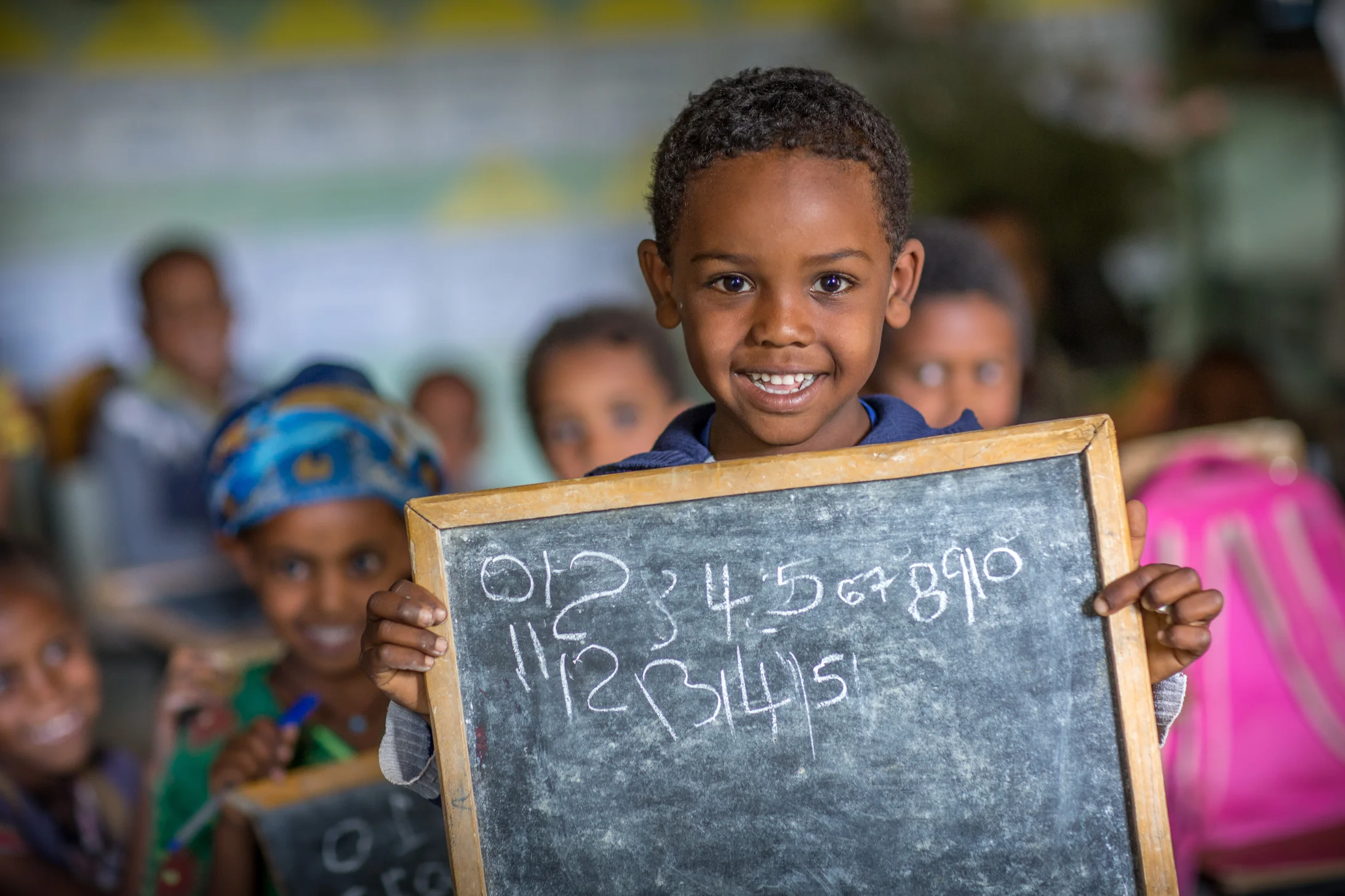 Enfant à l'école tenant une ardoise pleine d'écriture.