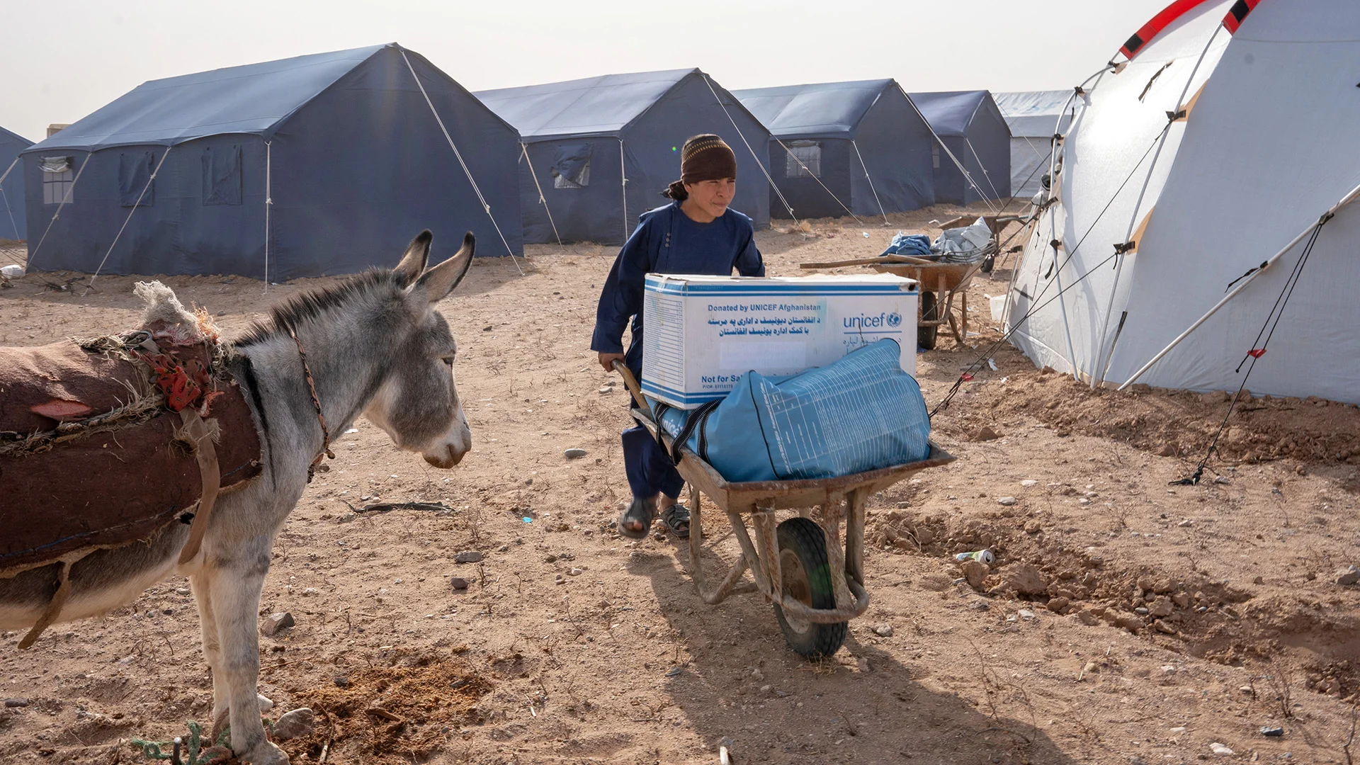 Ein Bub schiebt in einem Notlager in Afghanistan Hilfsgüter von UNICEF auf einem Schubkarren.