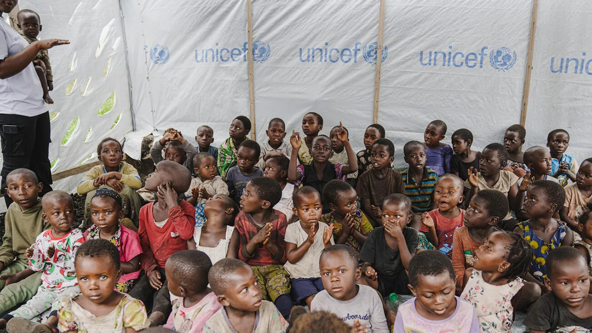 Viele Kinder sitzen auf dem Boden in einem UNICEF-Lernzelt und schauen in die Kamera.