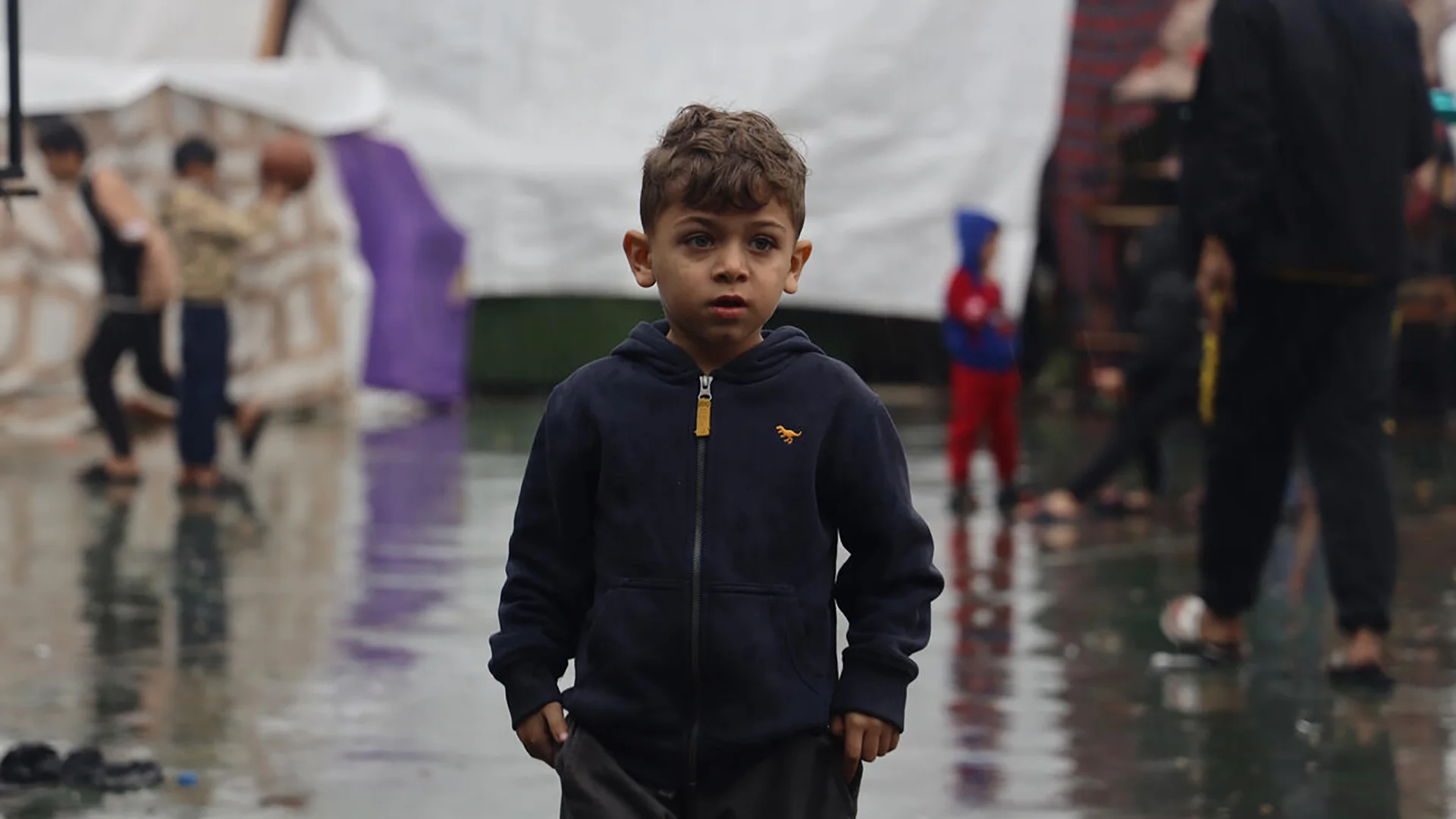 Ein kleiner Junge aus Gaza steht inmitten eines Zeltlagers im Regen.