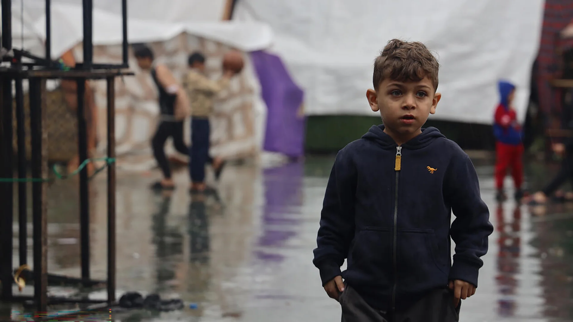 Ein kleiner Junge in Gaza steht inmitten von Notzelten im Regen.