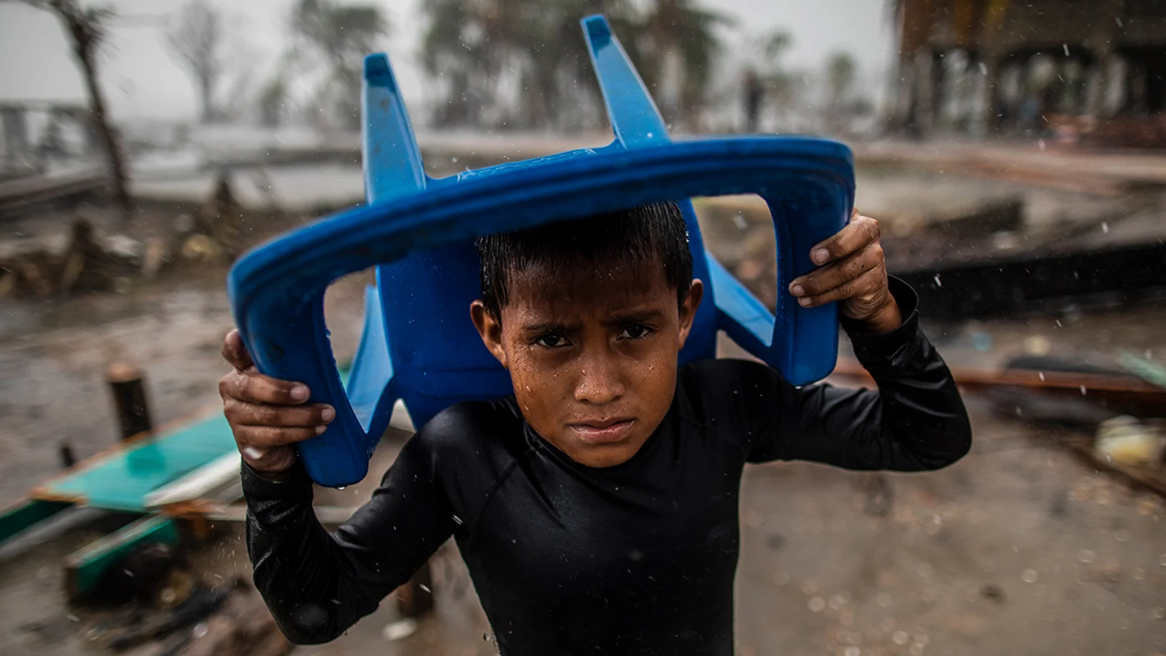 Le 17 novembre 2020 à Bilwi, au Nicaragua, un enfant se protège des fortes pluies avec une chaise en plastique, debout à l'endroit où se trouvait sa maison, après qu'elle ait été détruite par les vents violents, la houle et les pluies provoquées par l'ouragan Iota.