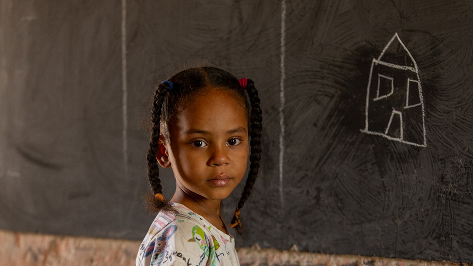 Ein kleines Mädchen aus dem Sudan steht vor einer Tafel.